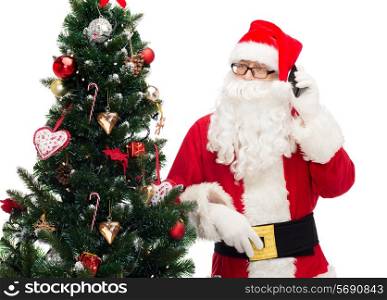 holidays, technology and people concept - man in costume of santa claus with smartphone and christmas tree
