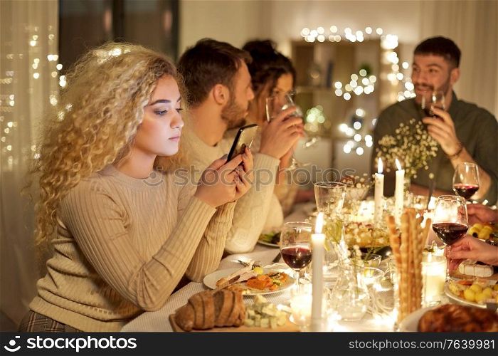 holidays, technology and people concept - sad young woman with smartphone at christmas dinner party with friends at home. woman with smartphone at dinner party with friends