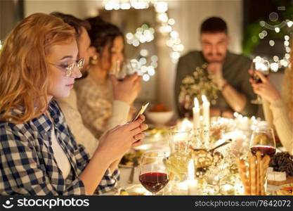 holidays, technology and people concept - young redhead woman in glasses with smartphone at christmas dinner party with friends at home. woman with smartphone at dinner party with friends