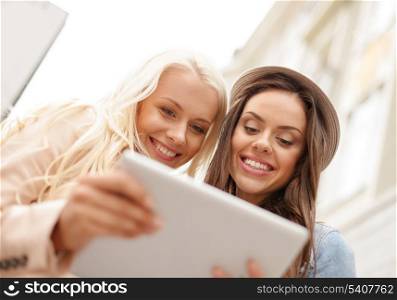 holidays, technology and tourism concept - two beautiful girls toursits looking into tablet pc in the city