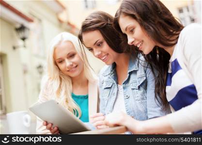 holidays, tourism and internet - beautiful girls looking at tablet pc in cafe outside