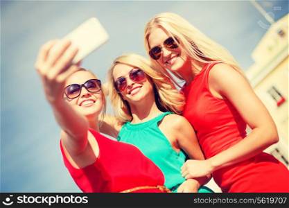 holidays, tourism and modern technology concept - smiling girls taking picture with smartphone camera in the city