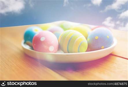 holidays, tradition and object concept - close up of colored easter eggs on plate over blue sky and clouds background