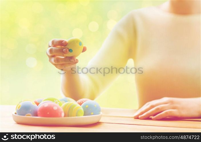 holidays, tradition and people concept - close up of woman hands with colored easter eggs on plate over green lights background