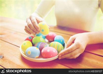 holidays, tradition and people concept - close up of woman hands with colored easter eggs on plate over green lights background. close up of woman hands with colored easter eggs