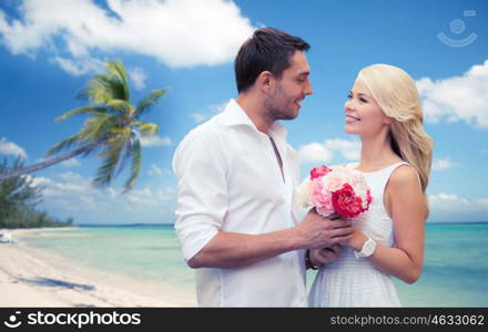 holidays, travel, tourism, people and dating concept - happy couple with bunch of flowers over tropical beach background