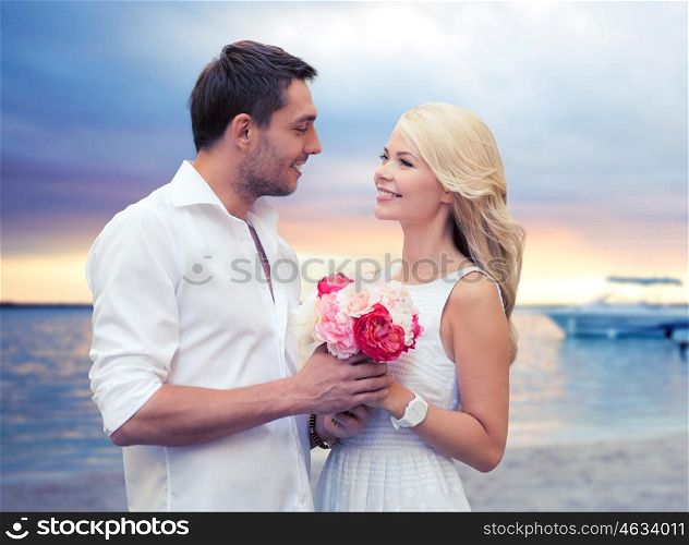holidays, travel, tourism, people and dating concept - happy couple with bunch of flowers over beach sunset background