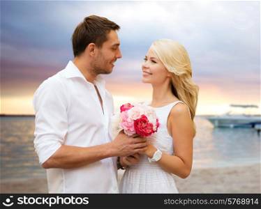 holidays, travel, tourism, people and dating concept - happy couple with bunch of flowers over beach sunset background