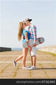 holidays, vacation and love concept - couple with skateboard kissing outdoors