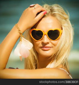 Holidays, vacation and summer fashion concept. Closeup attractive blonde girl in orange heart shaped sunglasses outdoor on beach water background