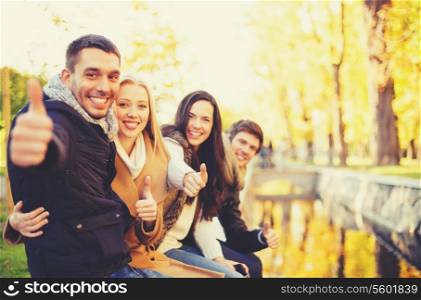 holidays, vacation, happy people concept - group of friends or couples having fun and showing thumbs up in autumn park