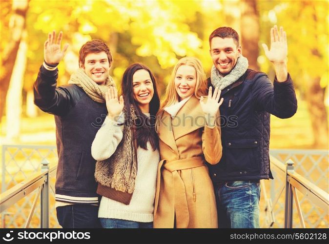 holidays, vacation, happy people concept - group of friends or couples having fun and waving hands in autumn park