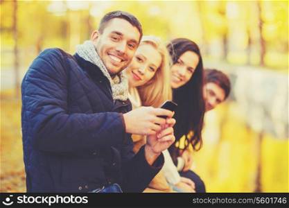 holidays, vacation, happy people concept - group of friends or couples with smartphone having fun in autumn park