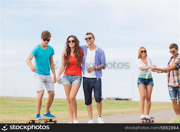 holidays, vacation, love and friendship concept - group of smiling teenagers walking and riding on skateboards outdoors