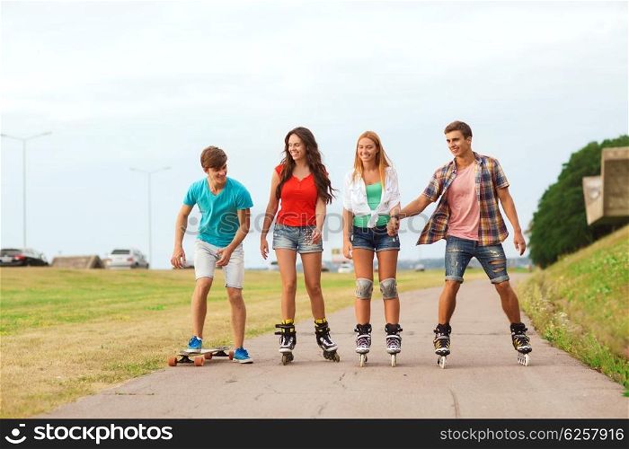 holidays, vacation, love and friendship concept - group of smiling teenagers with roller skates and skateboard riding outdoors