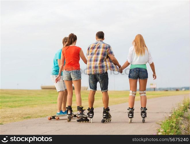 holidays, vacation, love and friendship concept - group of teenagers with roller skates and skateboard riding outdoors from back