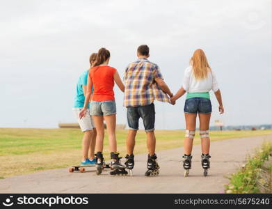 holidays, vacation, love and friendship concept - group of teenagers with roller skates and skateboard riding outdoors from back