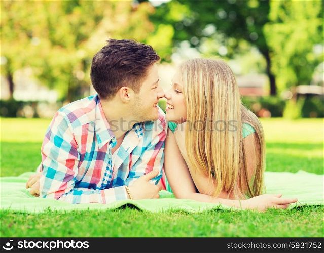 holidays, vacation, love and friendship concept - smiling couple lying on blanket and touching noses in park
