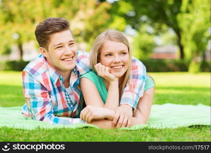 holidays, vacation, love and friendship concept - smiling couple lying on blanket in park