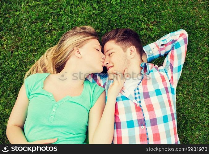holidays, vacation, love and friendship concept - smiling couple lying on on grass and kissing in park