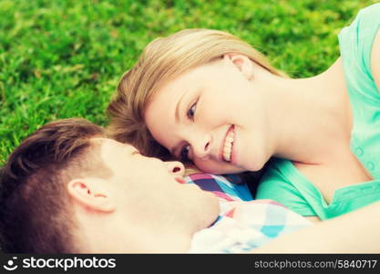 holidays, vacation, love and friendship concept - smiling couple lying on on grass in park