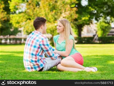 holidays, vacation, love and friendship concept - smiling couple sitting on grass and talking in park