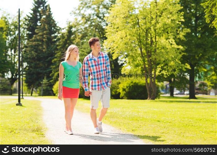 holidays, vacation, love and friendship concept - smiling couple walking and holding hands in park