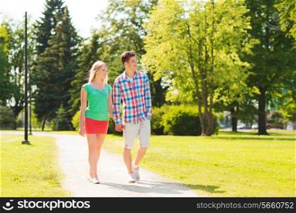 holidays, vacation, love and friendship concept - smiling couple walking and holding hands in park