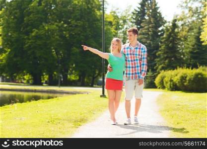 holidays, vacation, love and friendship concept - smiling couple walking and pointing finger in park