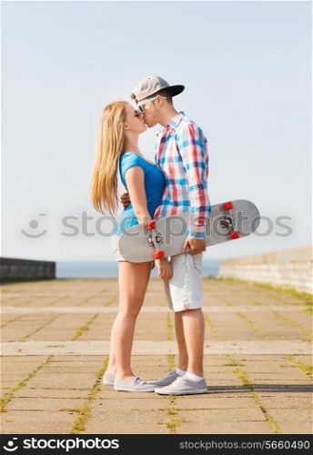 holidays, vacation, love and friendship concept - smiling couple with skateboard kissing outdoors
