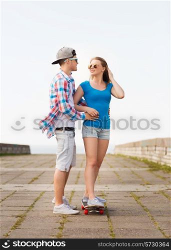 holidays, vacation, love and friendship concept - smiling couple with skateboard outdoors