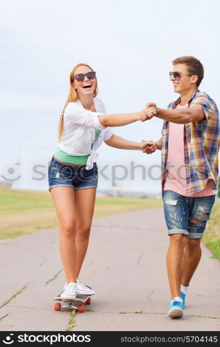 holidays, vacation, love and friendship concept - smiling couple with skateboard riding and holding hands outdoors