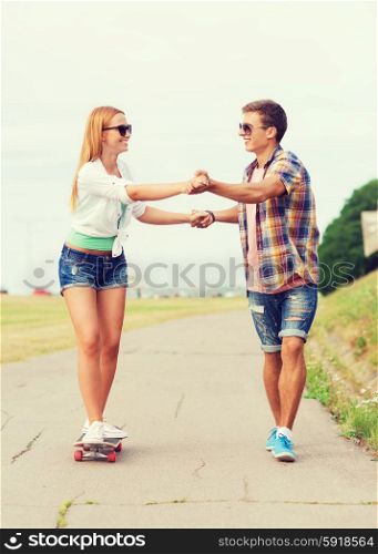 holidays, vacation, love and friendship concept - smiling couple with skateboard riding and holding hands outdoors