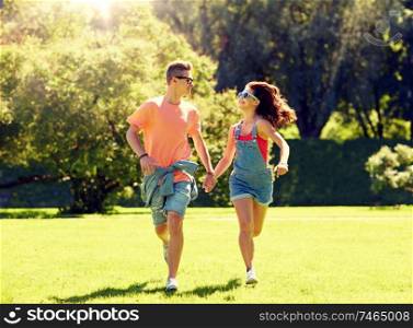 holidays, vacation, love and people concept - happy smiling teenage couple holding hands and running at summer park. happy teenage couple running at summer park