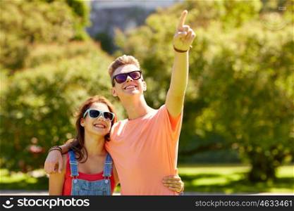 holidays, vacation, love and people concept - happy smiling teenage couple hugging and pointing finger to something at summer park