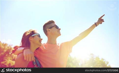 holidays, vacation, love and people concept - happy smiling teenage couple hugging and pointing finger up to something at summer. happy couple pointing finger at summer park