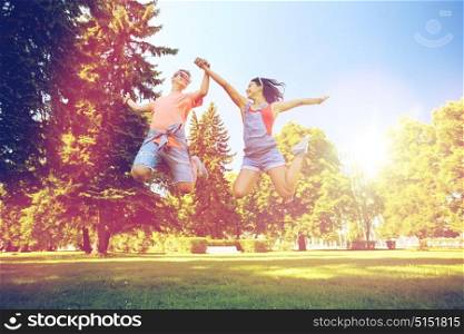 holidays, vacation, love and people concept - happy smiling teenage couple jumping at summer park. happy teenage couple jumping at summer park