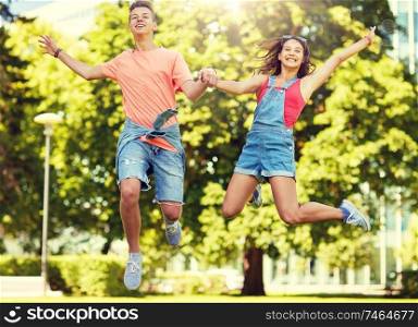 holidays, vacation, love and people concept - happy smiling teenage couple jumping at summer park. happy teenage couple jumping at summer park
