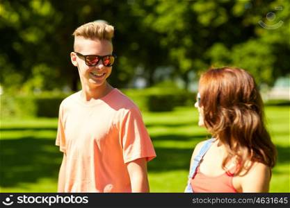 holidays, vacation, love and people concept - happy smiling teenage couple walking and looking at each other in summer park