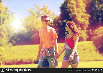 holidays, vacation, love and people concept - happy smiling teenage couple walking and looking at each other in summer park. happy teenage couple walking at summer park