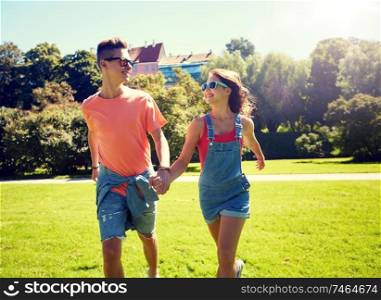holidays, vacation, love and people concept - happy smiling teenage couple walking and looking at each other in summer park. happy teenage couple walking at summer park