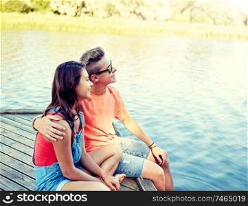 holidays, vacation, love and people concept - happy teenage couple hugging on river berth at summer. happy teenage couple hugging on river berth