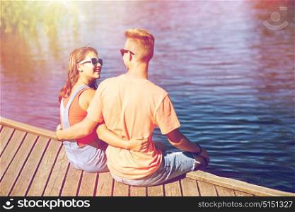 holidays, vacation, love and people concept - happy teenage couple sitting and hugging on river berth at summer. happy teenage couple hugging on river berth