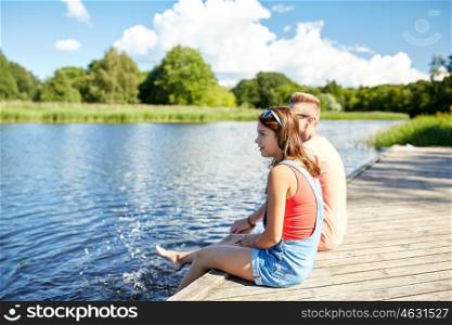 holidays, vacation, love and people concept - happy teenage couple sitting on river berth at summer