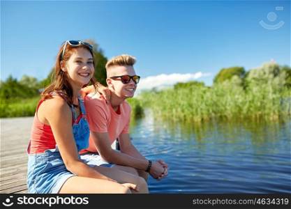 holidays, vacation, love and people concept - happy teenage couple sitting on river berth at summer