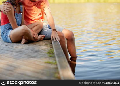 holidays, vacation, love and people concept - happy teenage couple sitting on river berth at summer