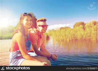 holidays, vacation, love and people concept - happy teenage couple sitting on river berth at summer. happy teenage couple sitting on river berth