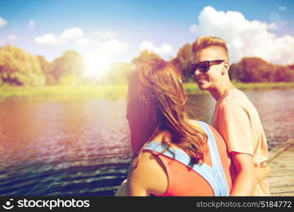 holidays, vacation, love and people concept - happy teenage couple sitting on river berth at summer. happy teenage couple sitting on river berth