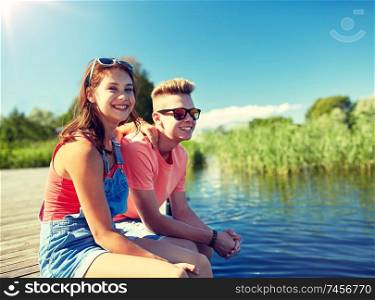 holidays, vacation, love and people concept - happy teenage couple sitting on river berth at summer. happy teenage couple sitting on river berth