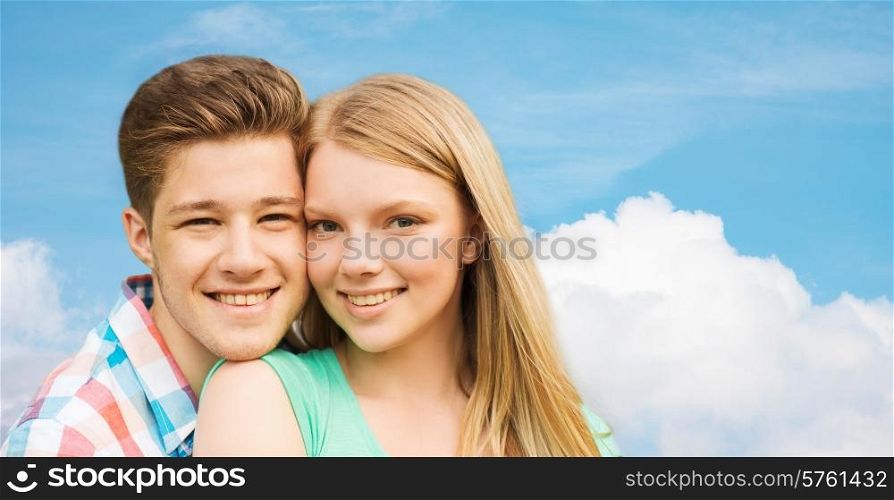 holidays, vacation, love and people concept - smiling teenage couple hugging over blue sky and cloud background